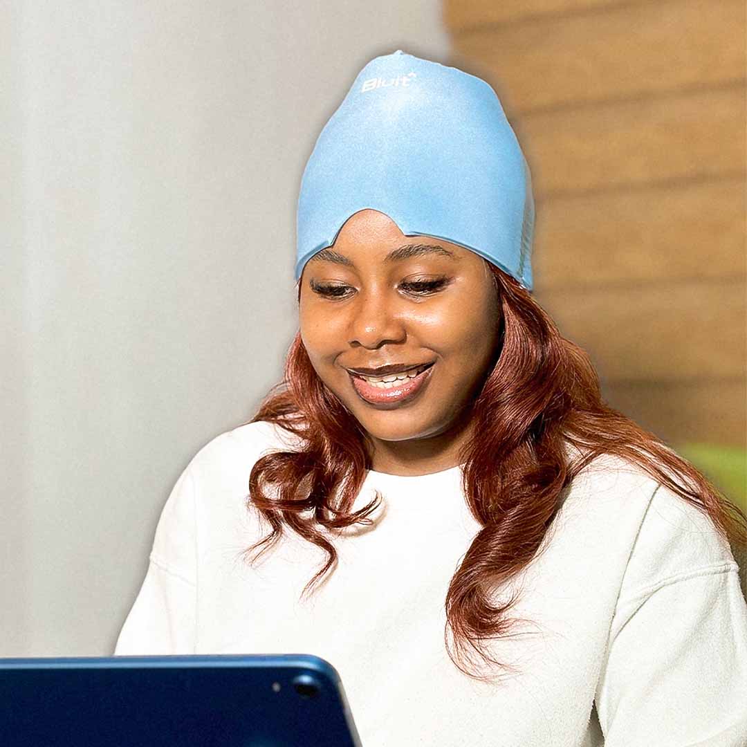 Woman wearing a blue Bluit Migraine Relief Cap while using a tablet